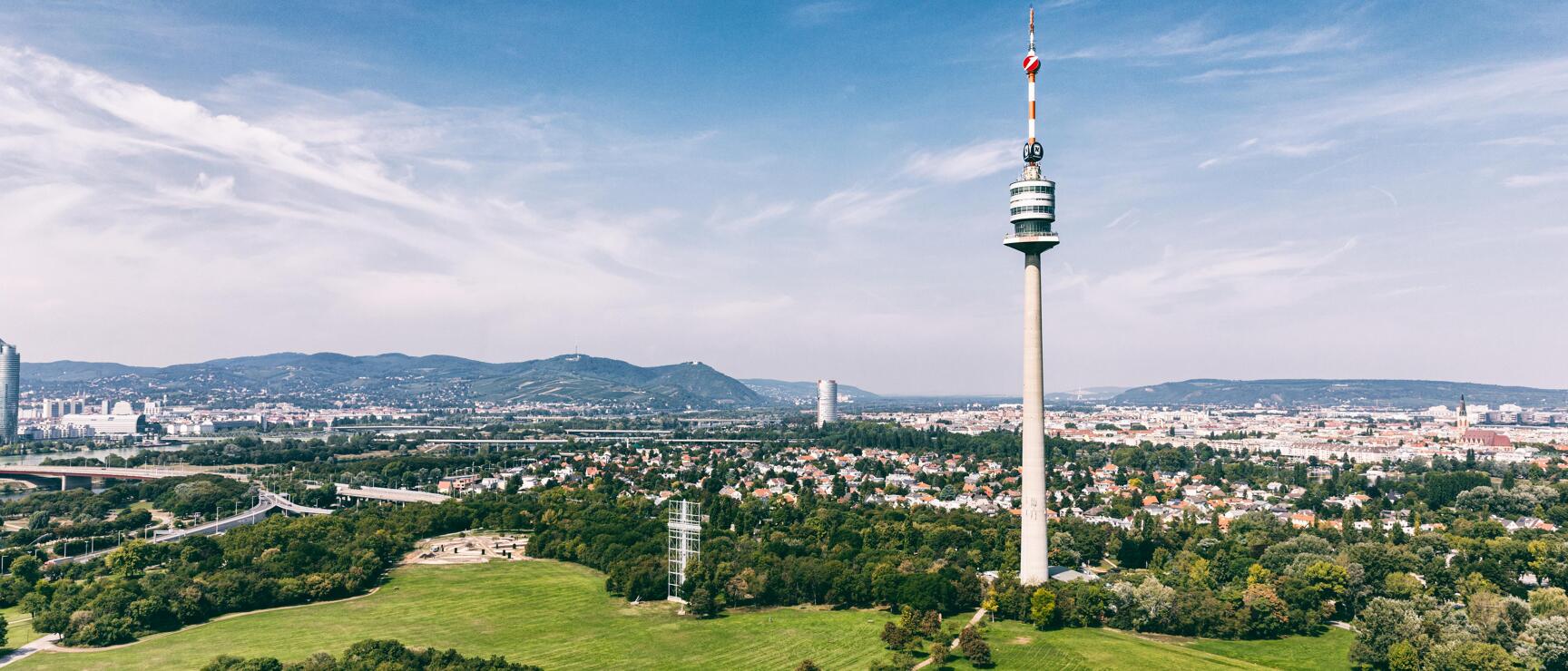 Danube Tower in Vienna's Danube Park with city panorama and Wienerwald forest in background, blue sky.