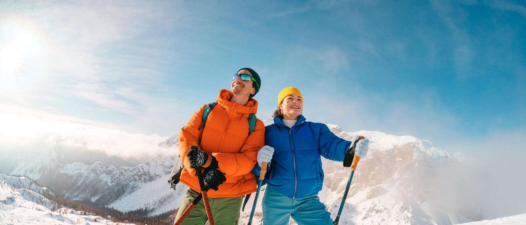Two snowshoers stand in a snow-covered mountain landscape, enjoying a winter day together in the Austrian Alps. The crisp air, bright sunlight, and sweeping views evoke a sense of freedom, a connection to nature, and a shared winter experience.