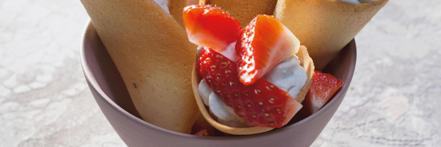 Palatschinken rolls with whipped cream and strawberries in a bowl, garnished with purple violets