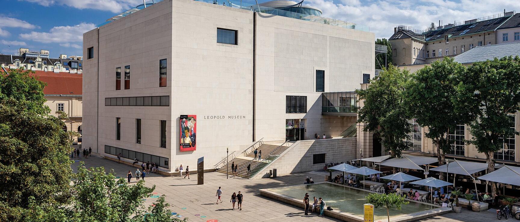 Leopold Museum Vienna in MuseumsQuartier, forecourt with fountain, sun umbrellas and visitors in summer weather.