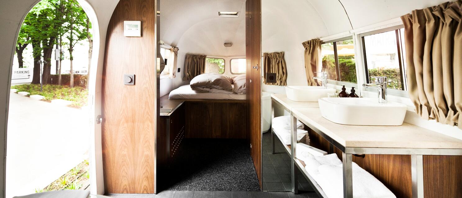 Innenraum eines Airstream-Wohnwagens mit zwei Waschbecken, Holzvertäfelung und Bett im Hintergrund.