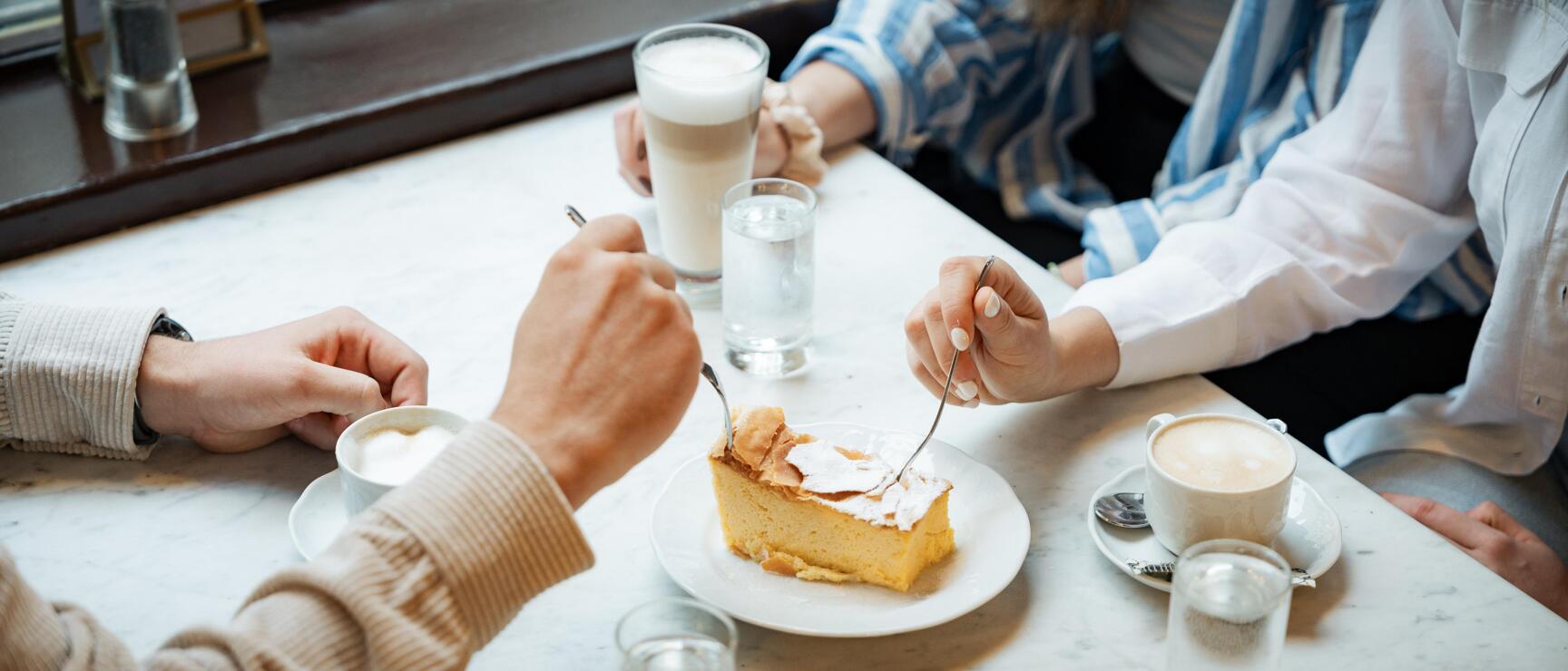 Two people sharing a piece of cake with powdered sugar, coffee and water on a marble table