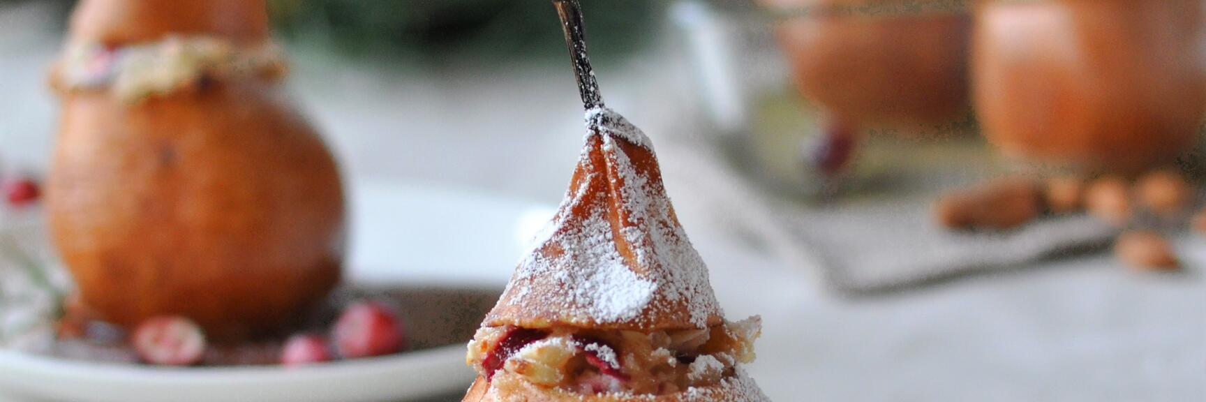 Baked pear with powdered sugar, cranberries and rosemary on white plate with two forks.
