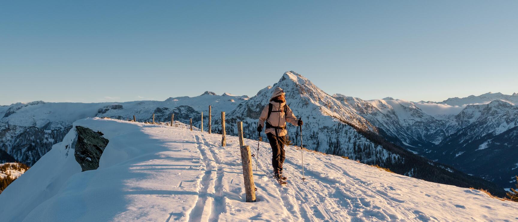 Ski tourer on a snow-covered ridge at Mooskopf in Kleinarl, with an impressive mountain panorama in the warm evening light.