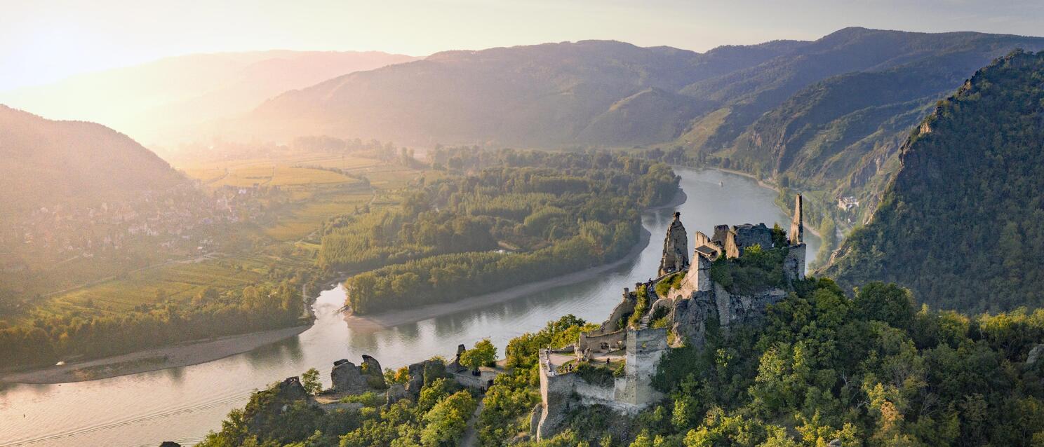 Ruins of Aggstein castle on forested rocks above the Danube in Wachau, hills in morning light.