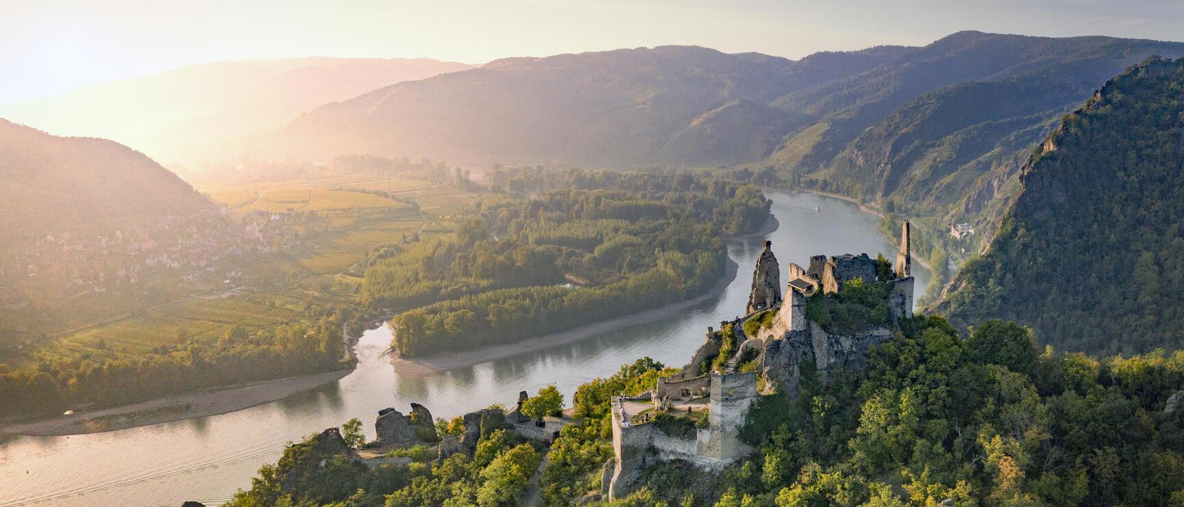 Ruins of Aggstein castle on forested rocks above the Danube in Wachau, hills in morning light.