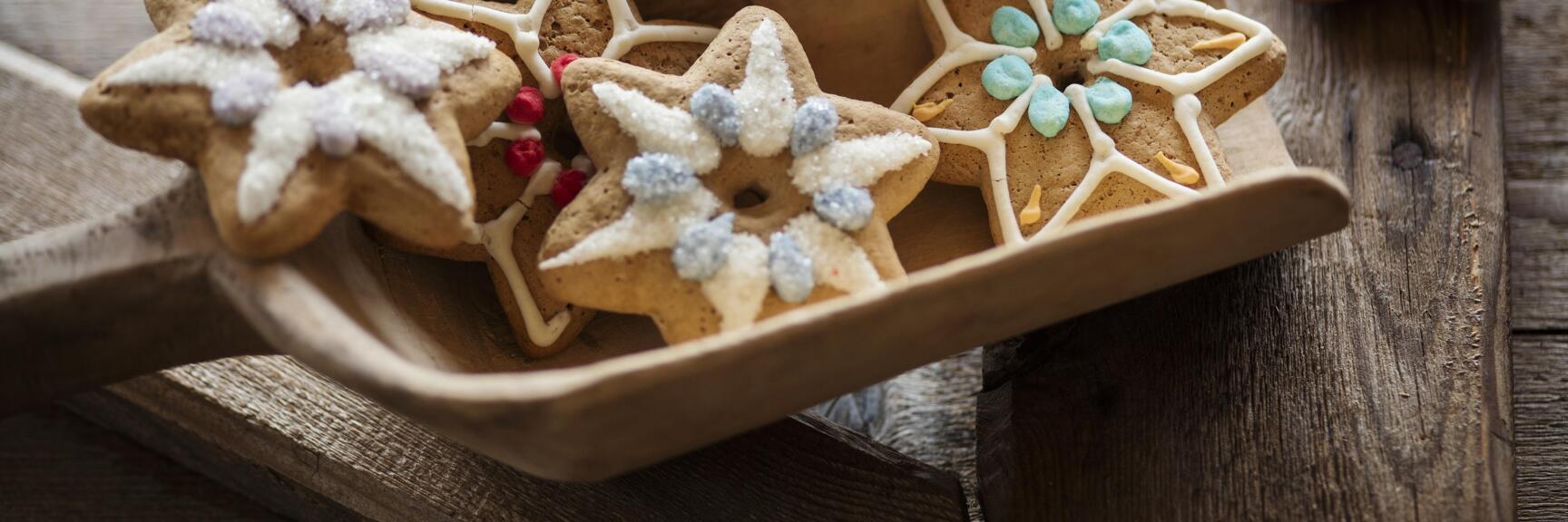 Star-shaped gingerbread cookies with colourful sugar glaze in a wooden bowl on a rustic wooden table.