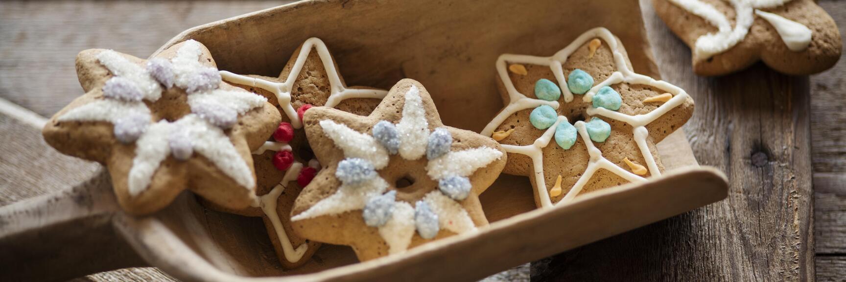 Sternförmige Lebkuchen mit bunter Zuckerglasur in einer Holzschale auf rustikalem Holztisch.