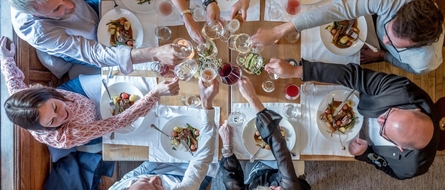 Overhead view of a group toasting with wine glasses at a set table with plates and food