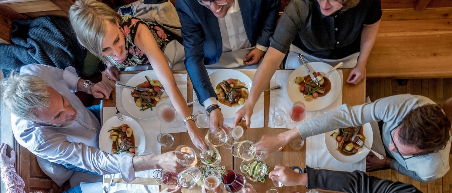 Overhead view of a group toasting with wine glasses at a set table with plates and food