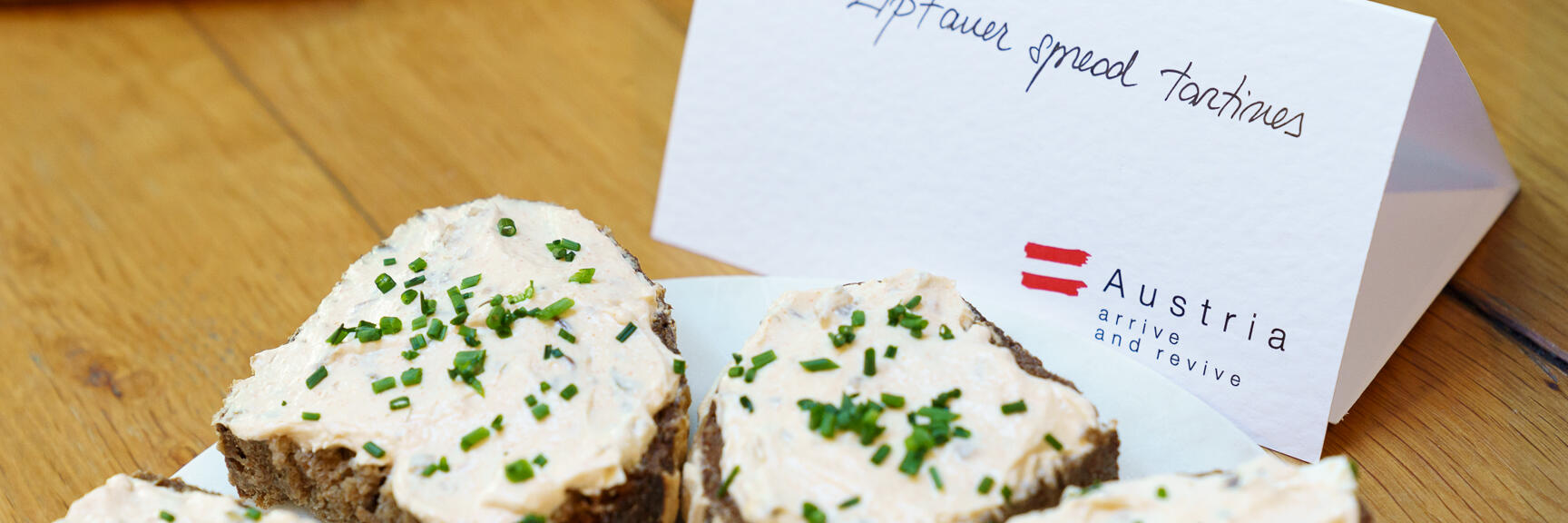 Bread slices with Liptauer spread and chives on plate, with labeled card beside.