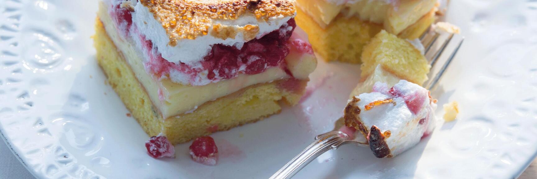 Two slices of sheet cake with berries and toasted meringue layer on white plate with fork.