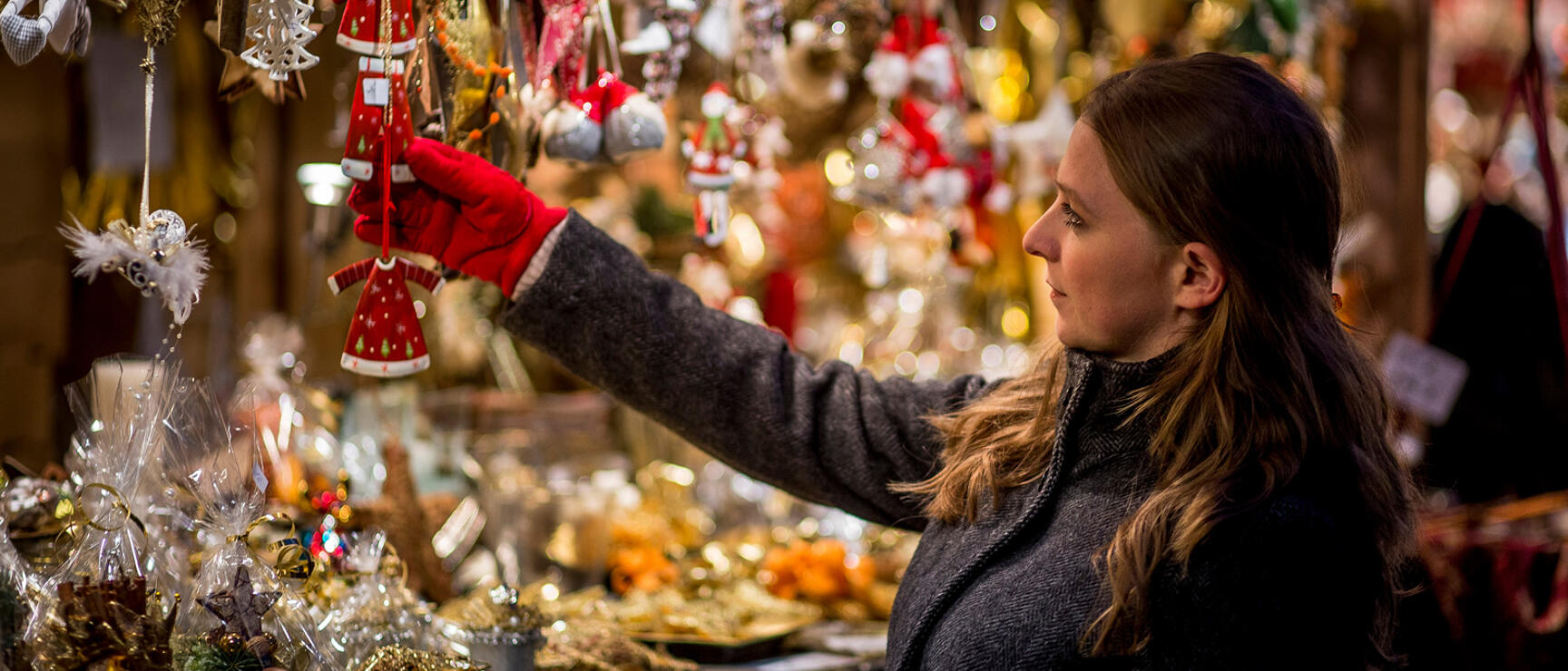 Woman in red gloves reaching for Christmas ornaments at an illuminated market stall