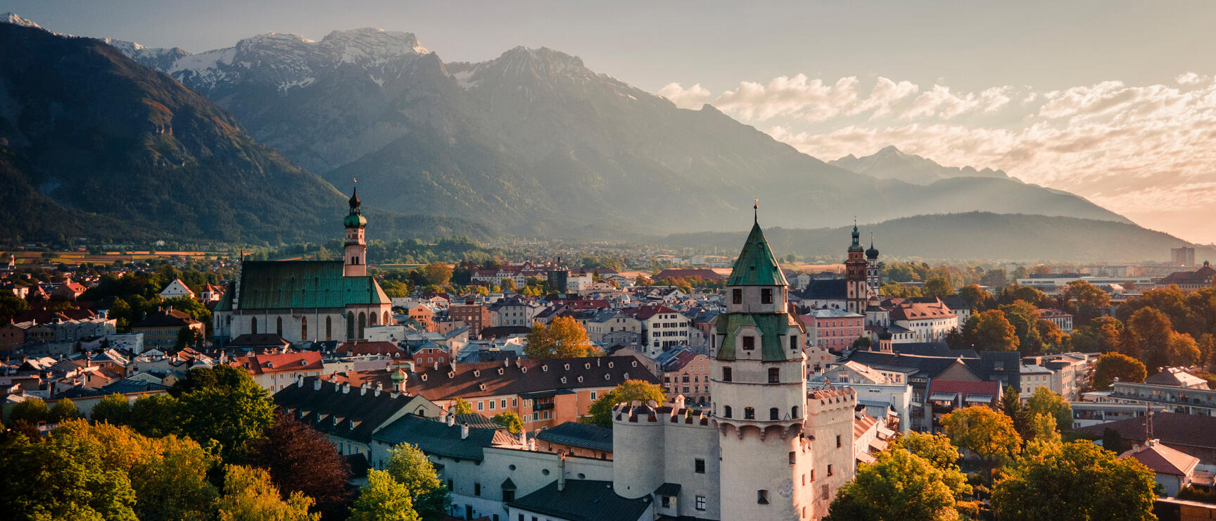 Aerial view of Hall in Tirol's old town with Münzer Tower, church spires and snow-capped mountains in the background.