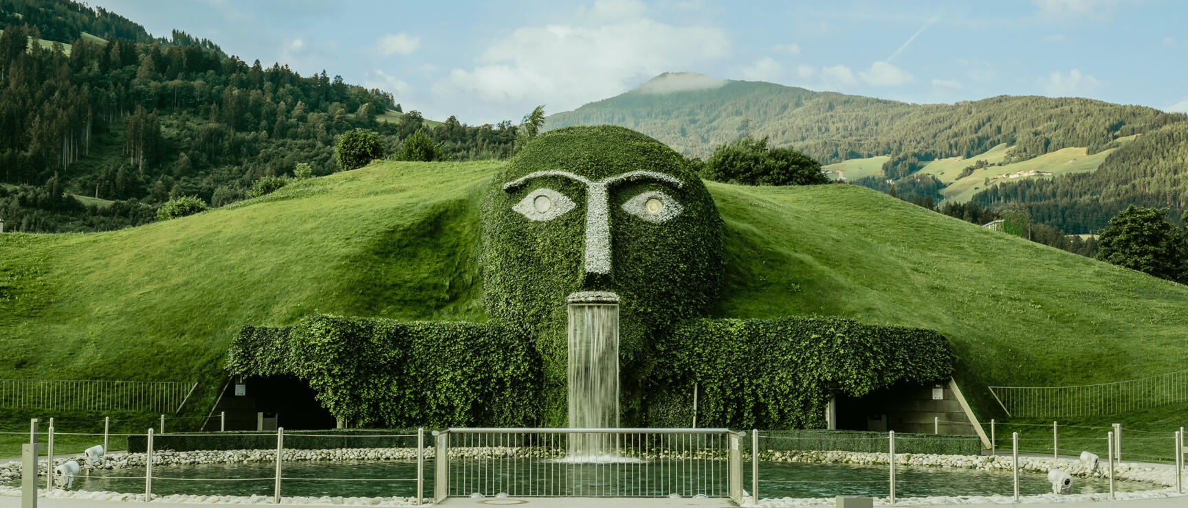 Giant green head with waterfall at Swarovski Kristallwelten in Wattens, Tyrolean mountain landscape in the background.