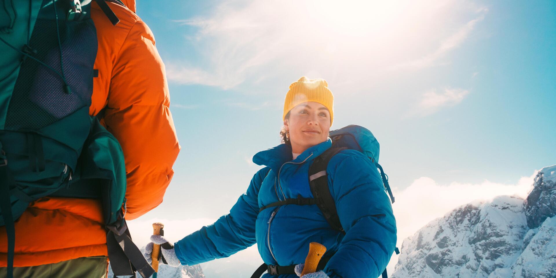 Zwei Personen beim Schneeschuhwandern in den verschneiten Bergen Österreichs. Vor der beeindruckenden Winterkulisse genießen sie die klare Bergluft, die strahlende Wintersonne und das Gefühl von Freiheit inmitten der alpinen Natur.