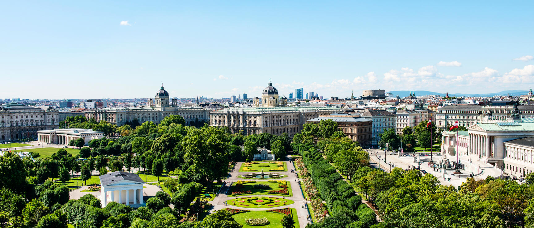 Aerial view of Vienna's Volksgarten with flower beds, Parliament building, and Museum of Art History in the background.