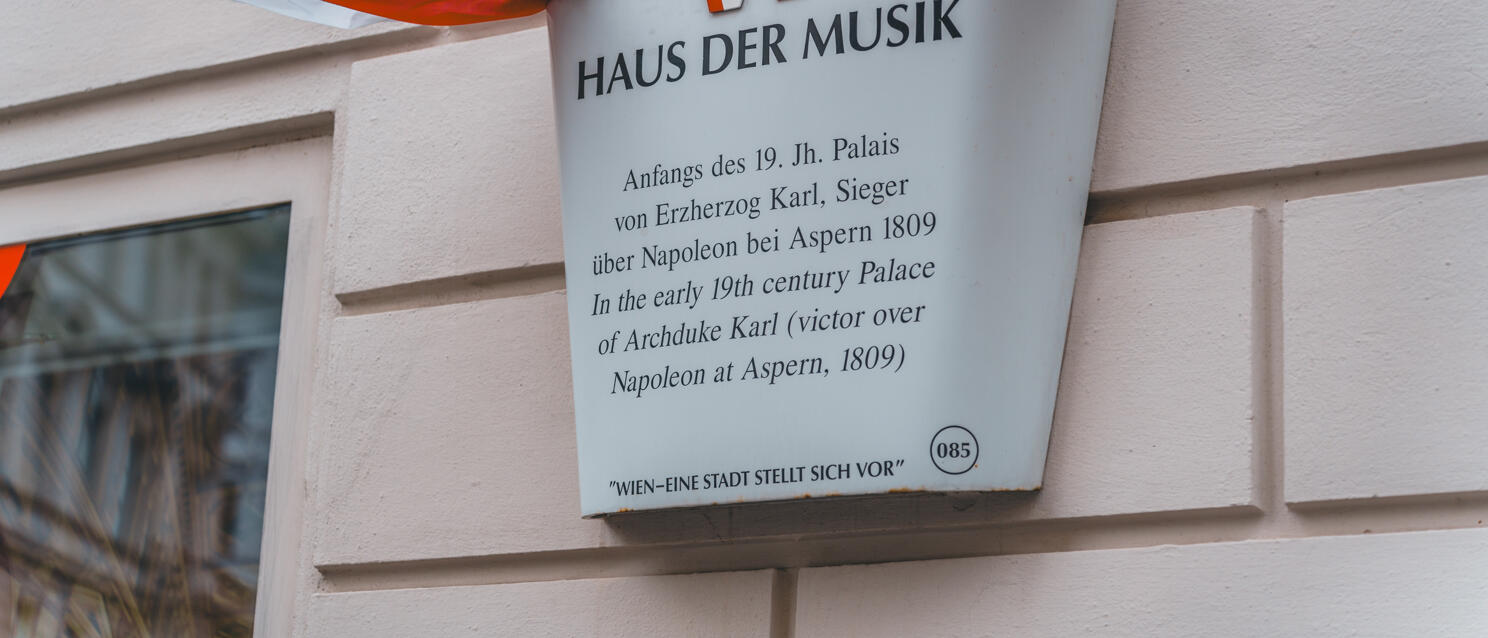 Signpost "House of Music" on a building facade in Vienna, red and white ribbons in the background.