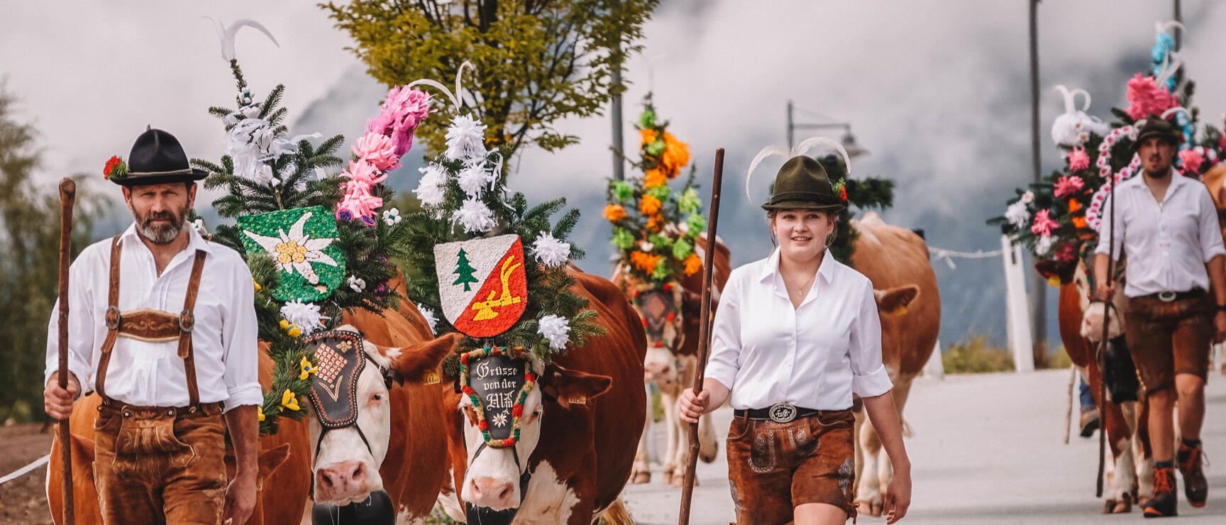 During the Almabtrieb in Reith im Alpbachtal, a man and a woman lead two decorated cows through the village; in the background, other people are seen with decorated cows