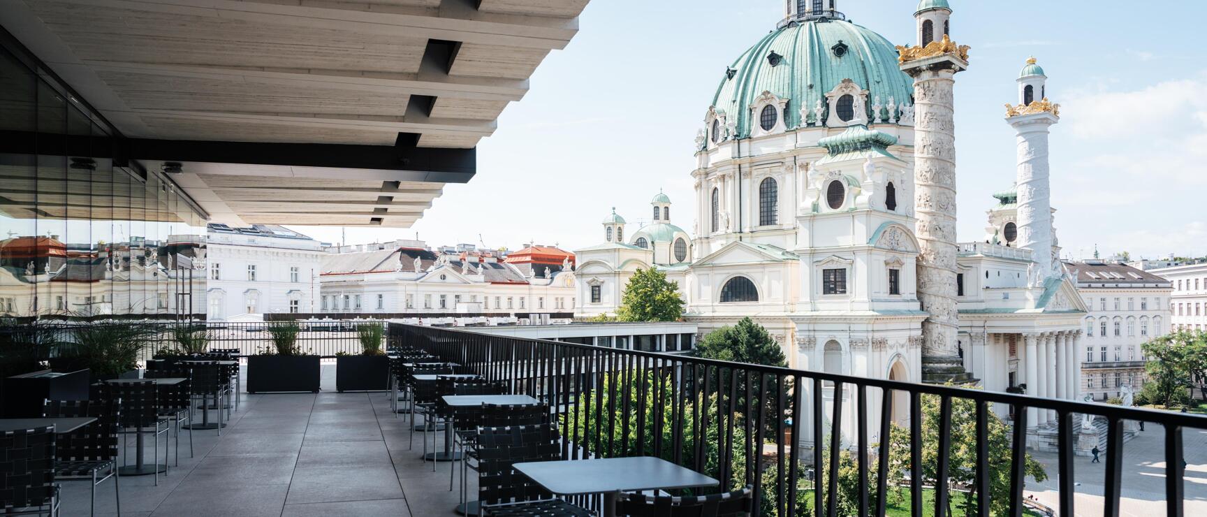 Empty terrace with tables and chairs overlooking Karlskirche with green dome, Vienna