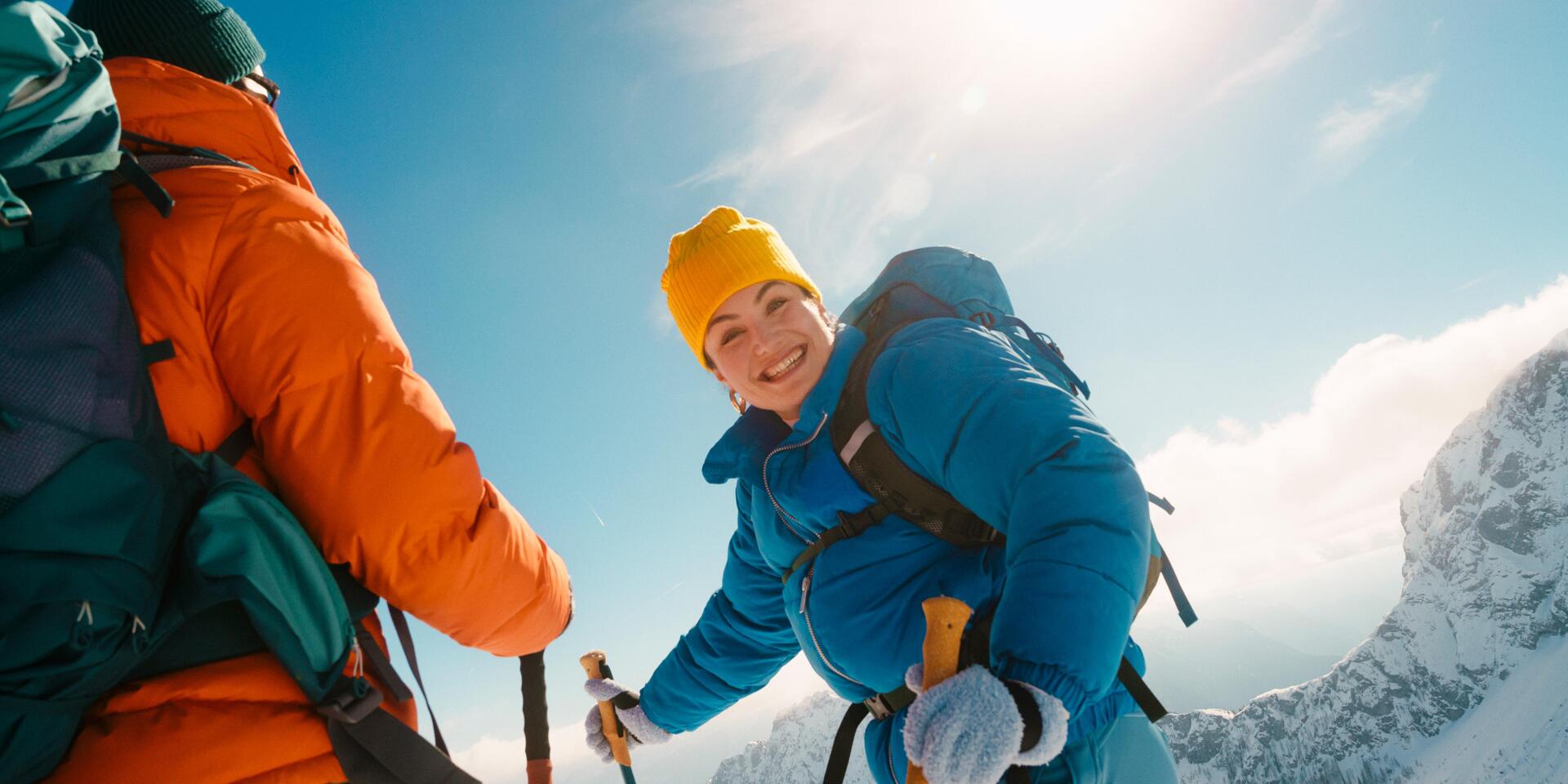 Two people snowshoeing in the Austrian mountains. Under the bright winter sun, they enjoy the snow-covered landscape, the crisp mountain air, and moments together filled with lightheartedness and joie de vivre.