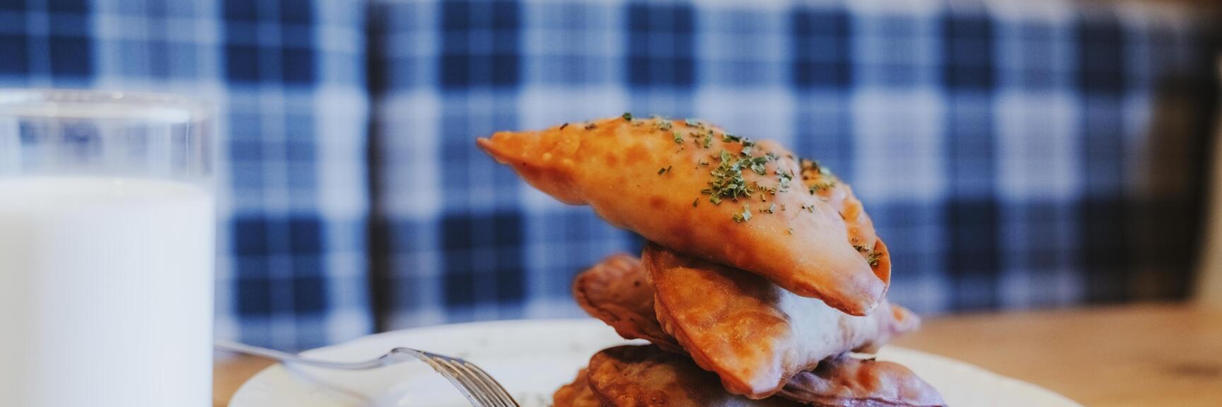 Stacked baked pastry pockets with herbs on white plate, fork and glass of milk beside it.