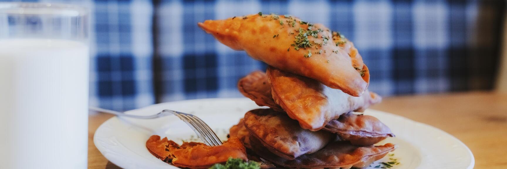 Stacked baked pastry pockets with herbs on white plate, fork and glass of milk beside it.