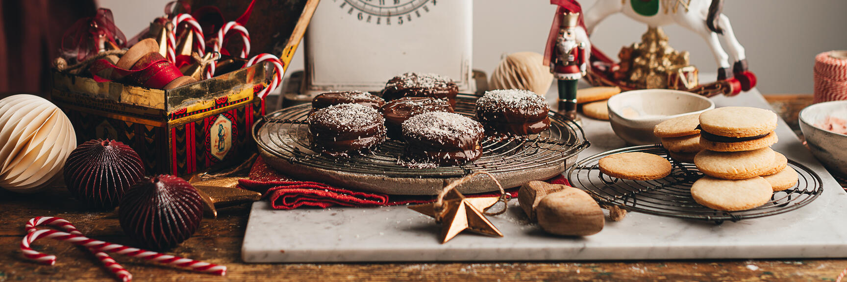 Christmas cookies on cooling racks, vintage kitchen scale, candy canes and Christmas decorations on wooden table.