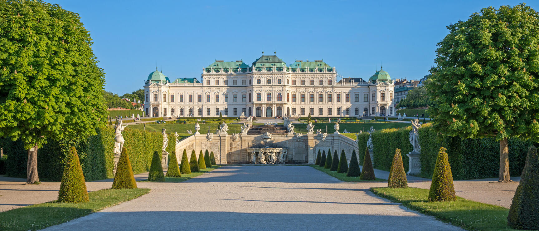View through the garden to Belvedere Palace in Vienna, with cone-shaped hedges, statues and blue sky.
