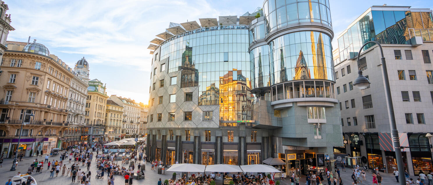 Bustling Stephansplatz in Vienna with modern glass buildings and historic architecture in evening light.