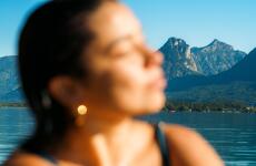 Woman in foreground (out of focus), blue lake and mountain peak beyond under clear sky.