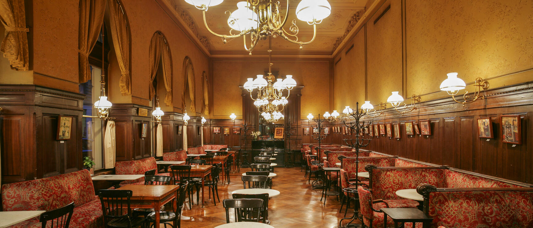 Historic Viennese coffee house with marble tables, red upholstered benches, wood panelling and chandeliers.