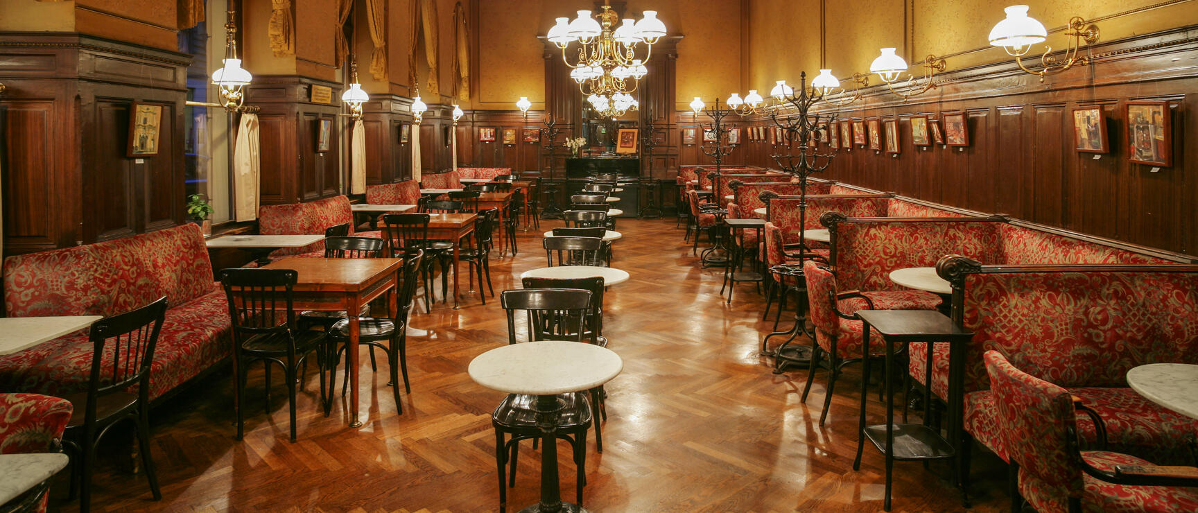 Historic Viennese coffee house with marble tables, red upholstered benches, wood panelling and chandeliers.