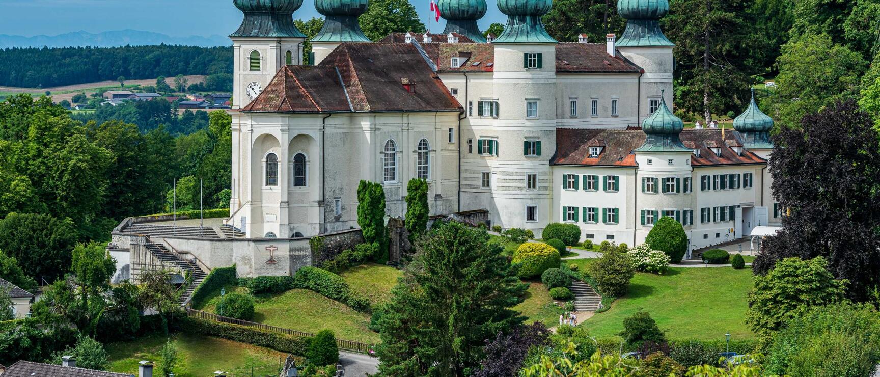 Artstetten Castle with white façade, green onion domes and castle church, surrounded by a park.