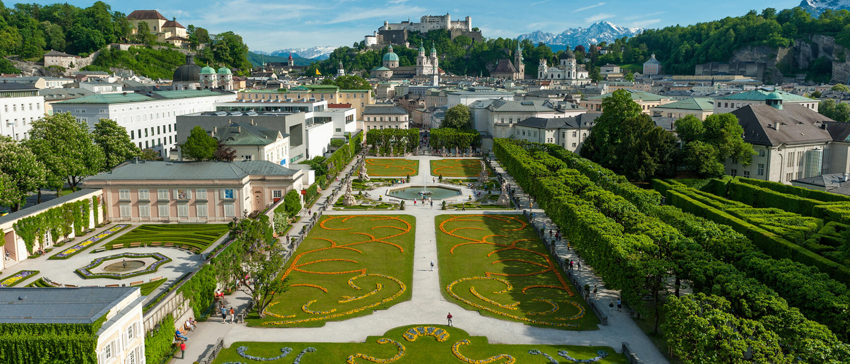 Mirabelle Garden Salzburg with flower beds, Hohensalzburg Fortress and Alps in background.