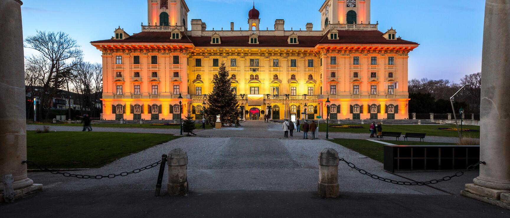 Esterházy Castle in Eisenstadt, orange-lit at dusk, illuminated Christmas tree in front of entrance.
