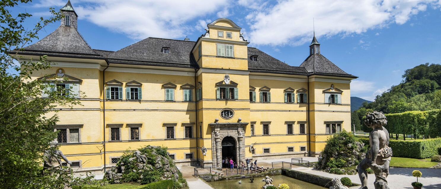 Hellbrunn Palace near Salzburg with yellow façade, Baroque statues, water basins and well-maintained garden park.