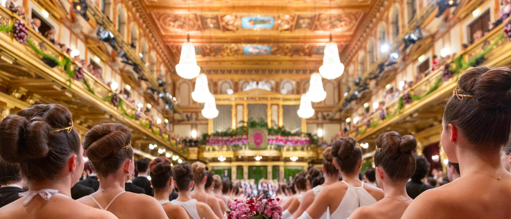 Debutantes in white dresses with rose bouquets in the Golden Hall of Vienna Music Society.
