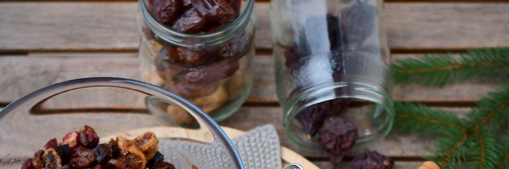 Glass bowl with dried fruit, red apples, nuts and raisins on wooden board, fir branches as decoration.