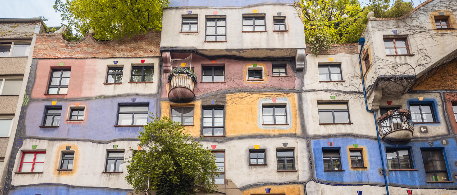 Colourful facade of Hundertwasser House in Vienna with irregular windows, coloured accents and trees.