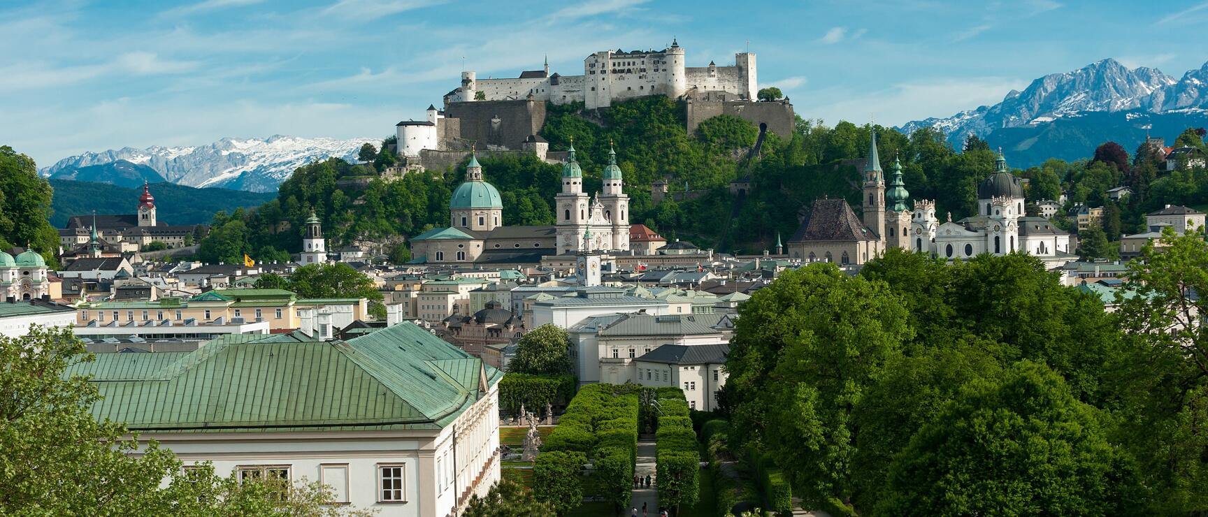 View over Mirabell Palace and Salzburg old town, Hohensalzburg Fortress and snow-capped Alps in background.