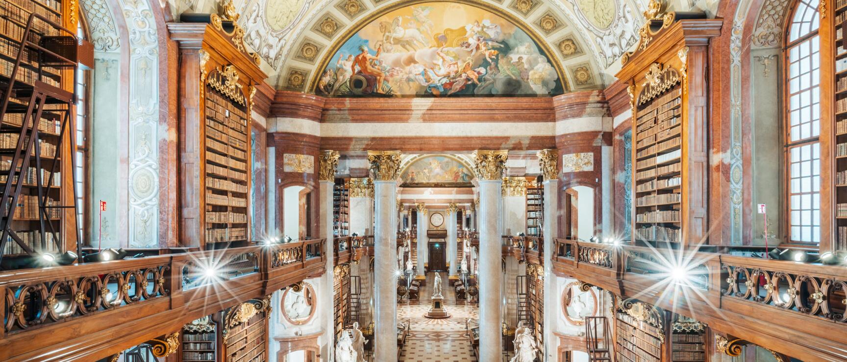 Grand Hall of Austrian National Library Vienna: bookshelves, marble columns, statues, ceiling fresco.