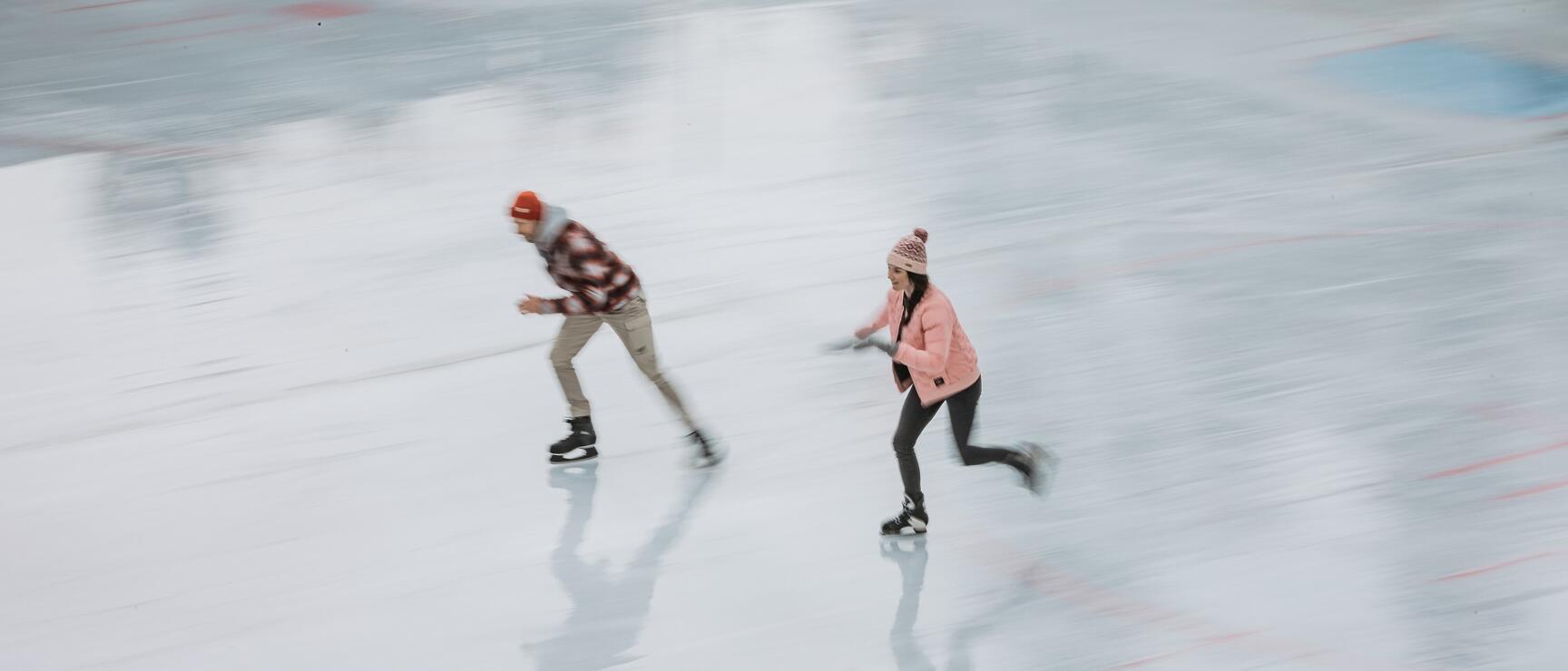Two people in woolly hats running fast on ice with motion blur visible.