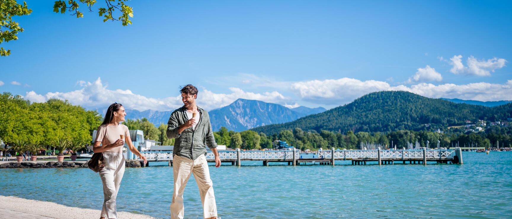 Couple walking along the eastern bay of Lake Wörthersee with a view of the Karawanken mountains