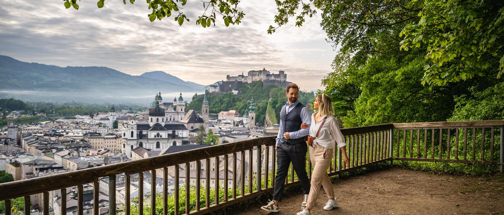 Couple at viewpoint overlooking Salzburg's old town and Hohensalzburg Fortress in the background