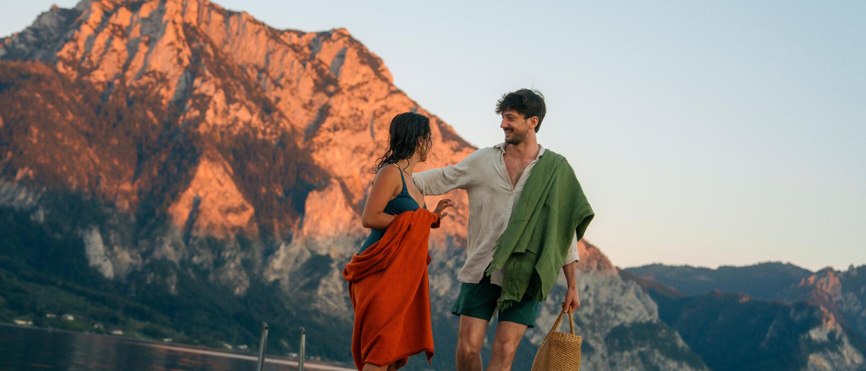 Couple on a wooden jetty at Traunsee lake, evening light on Traunstein mountain in the background.