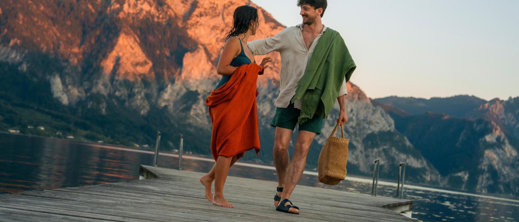 Couple on a wooden jetty at Traunsee lake, evening light on Traunstein mountain in the background.