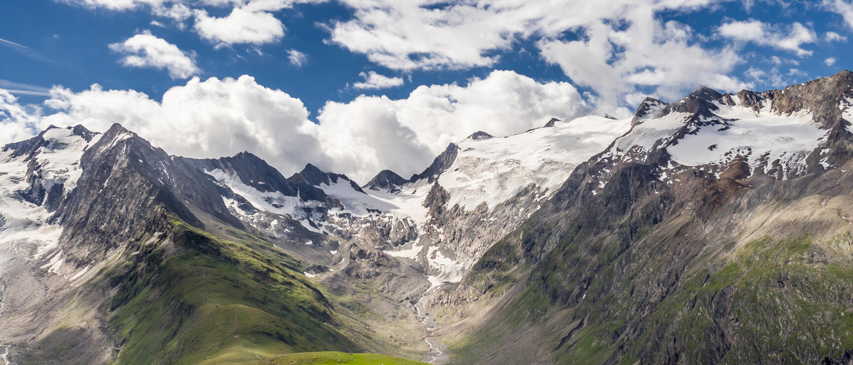 Alpine hut on green high meadow with glaciated mountains and glacier tongue in background under blue sky