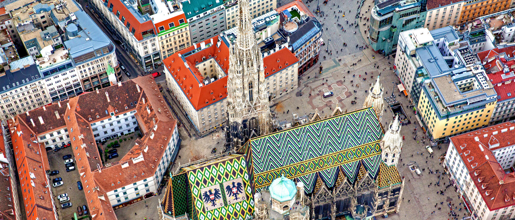 Aerial view of St. Stephen's Cathedral with colorful tile roof and North Tower surrounded by Vienna's inner city buildings.