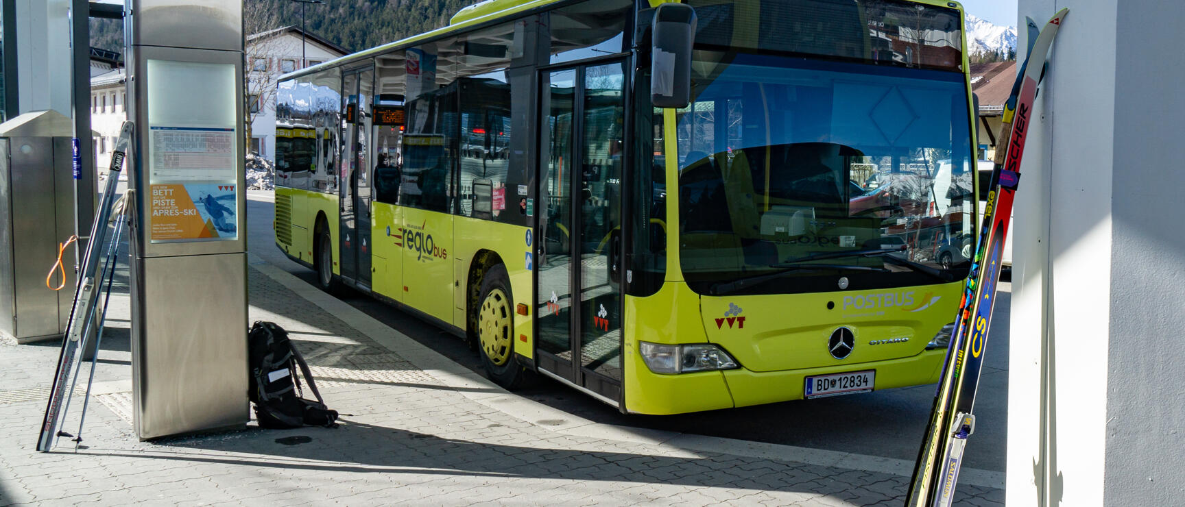 Yellow regional bus at stop C in Seefeld in Tirol, ski equipment in foreground, mountain in background.